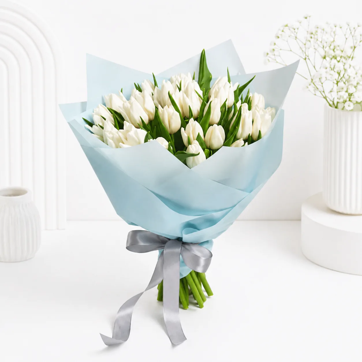 Elegant bouquet of fresh white tulips wrapped in pastel blue paper with a silver ribbon, perfect for gifting in Dubai by Favish Blooms