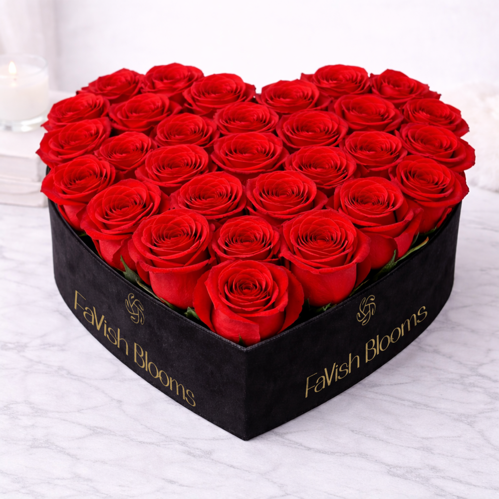 Red roses arranged in a black heart-shaped gift box on a marble surface.