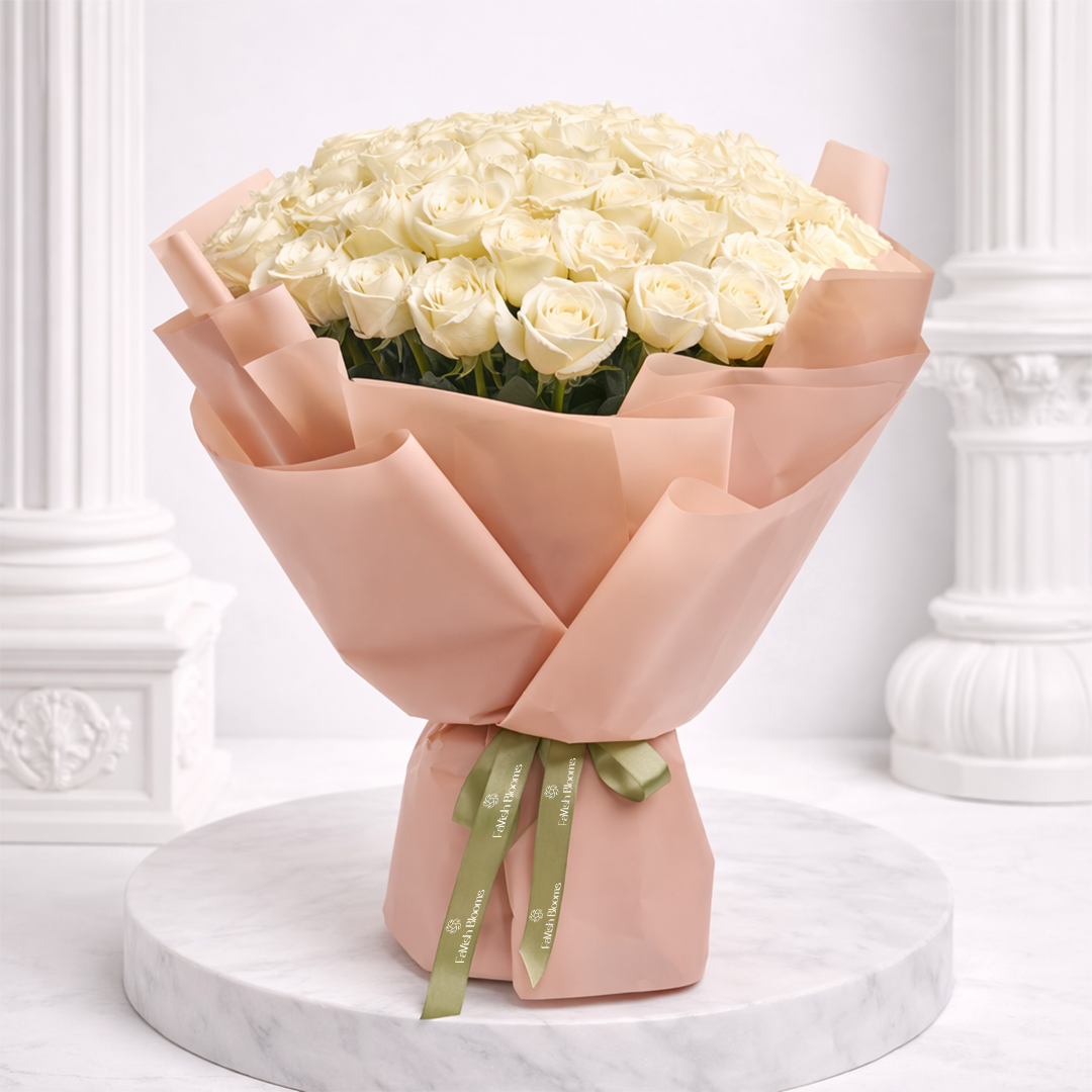 A large bouquet of white roses wrapped in blush pink paper, tied with a green branded ribbon.