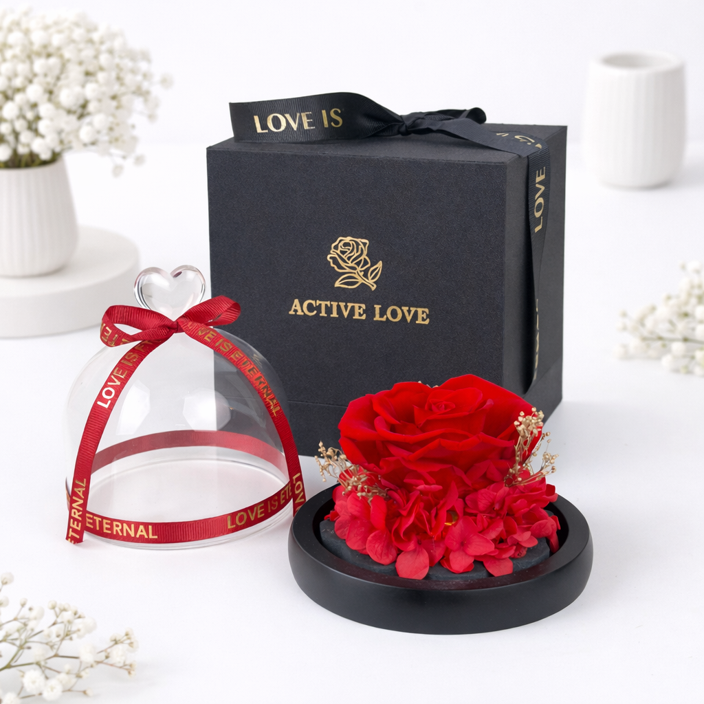 A preserved red rose under a glass dome with a heart handle and red ribbon, beside an "Active Love" black gift box.