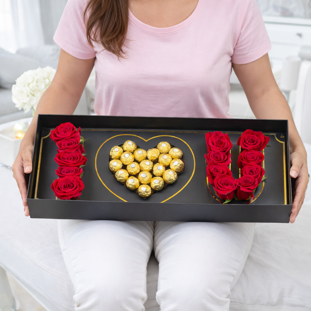 Woman holding a black gift box with red roses and Ferrero Rocher chocolates arranged in "I ♥ U".