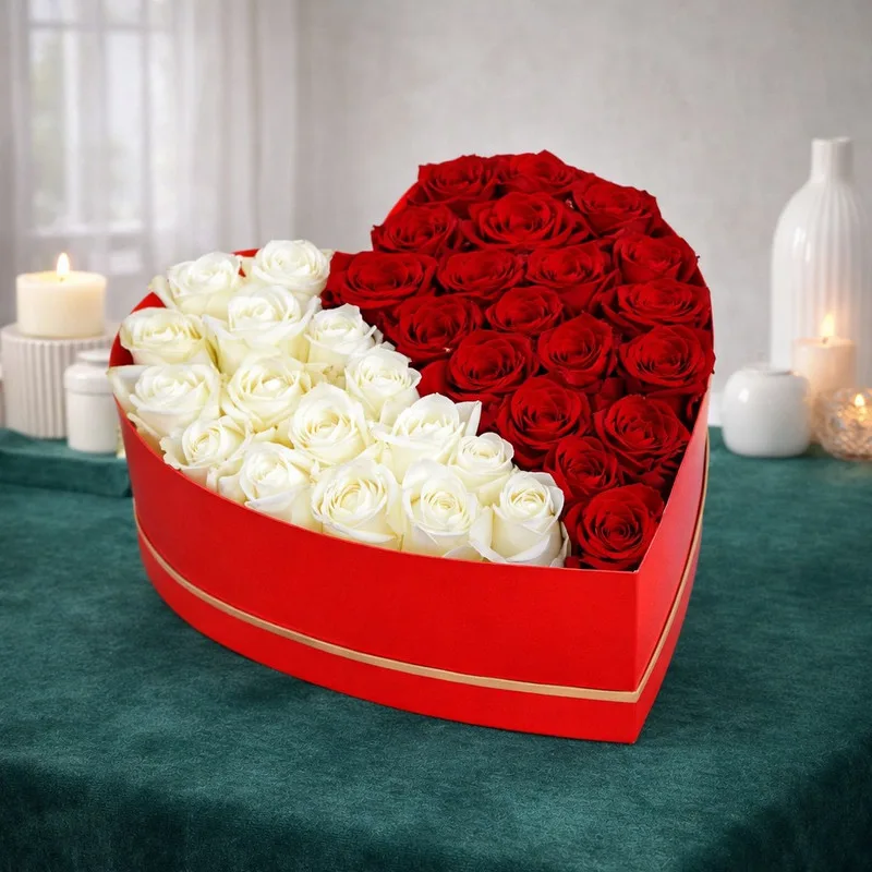 Red and white roses arranged in a heart-shaped red gift box with gold trim.