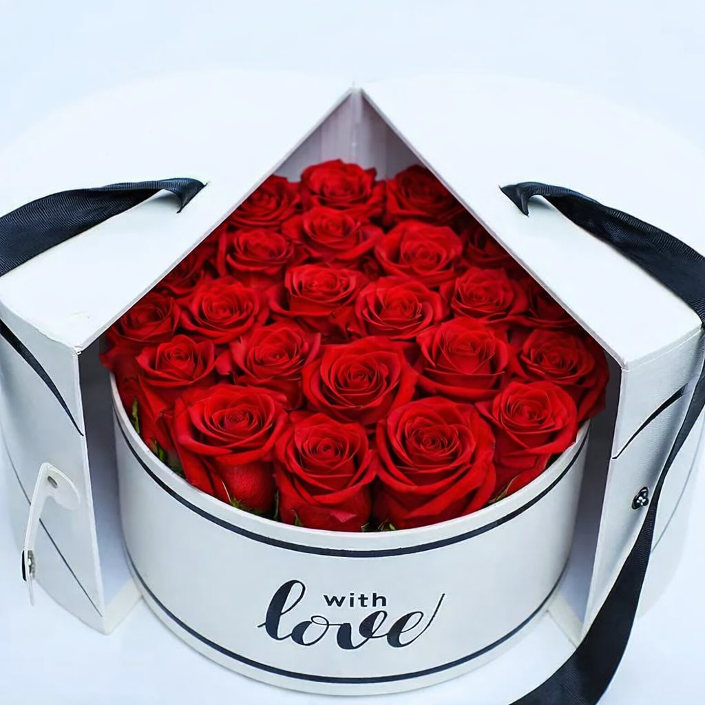 Close-up of red roses inside an open white "With Love" round gift box with black ribbon handles.