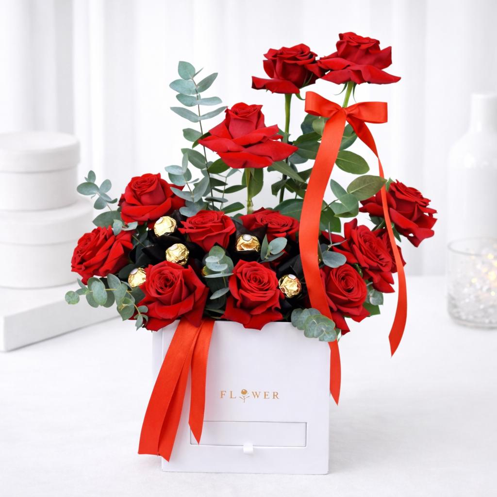 Red roses and Ferrero Rocher chocolates with eucalyptus in a white gift box tied with a red ribbon.
