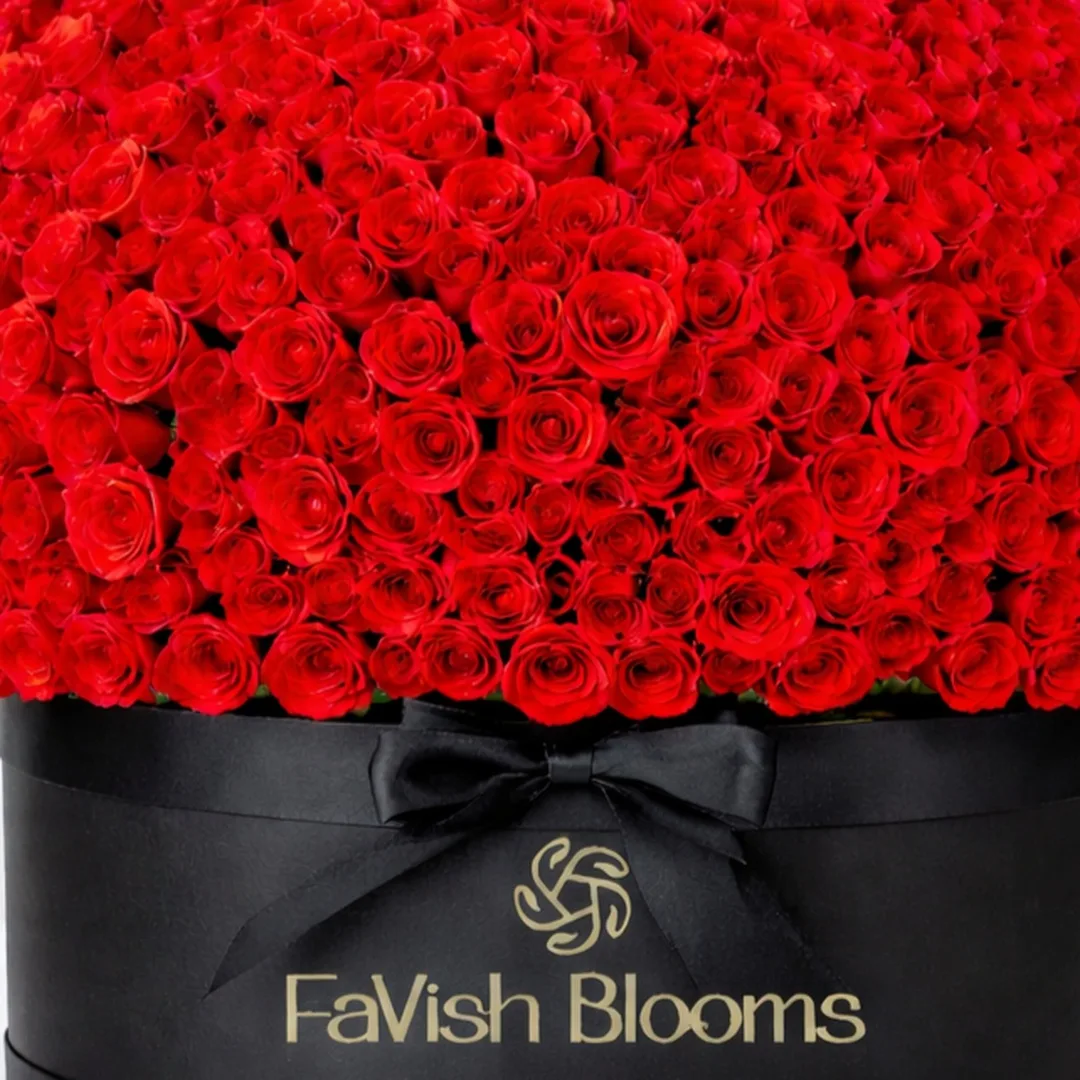 Close-up of a dome-shaped red rose arrangement in a black FaVish Blooms hatbox with a satin bow.