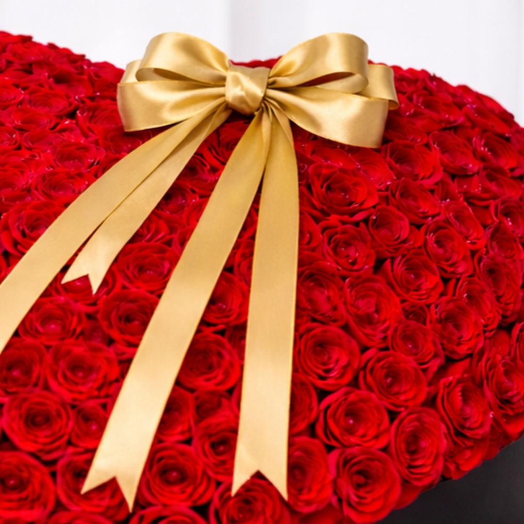 Close-up of a heart-shaped red rose arrangement with a gold satin bow in a black box
