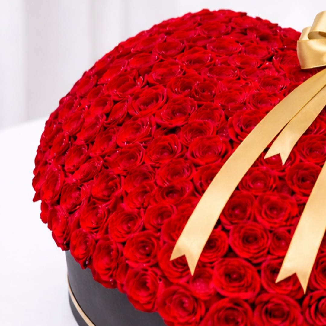 Hundreds of red roses arranged in a black hatbox with a gold ribbon bow.