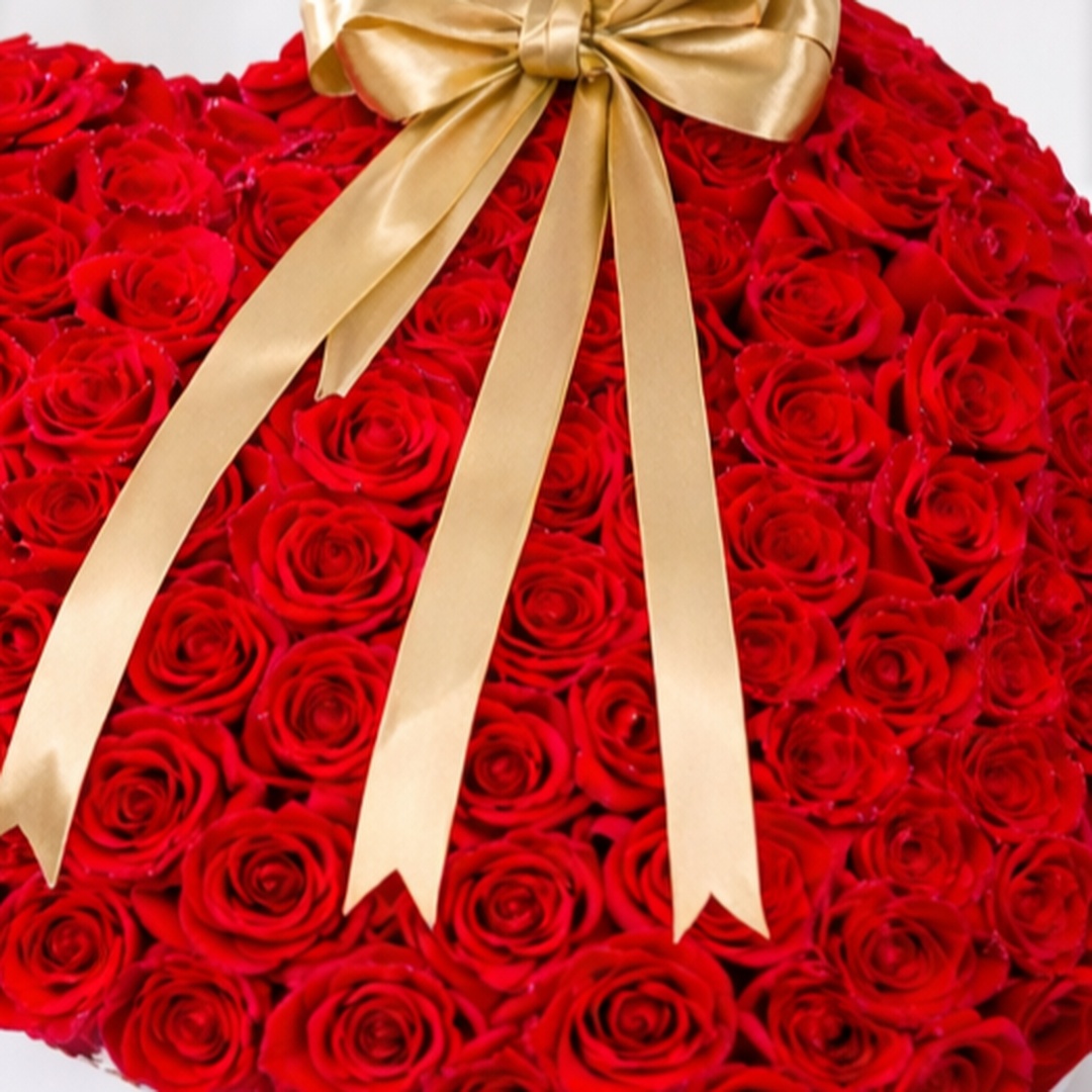 Close-up of a heart-shaped red rose arrangement with a gold satin bow