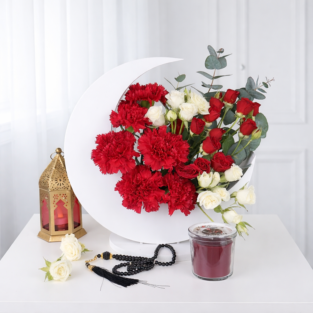A wide shot of a white crescent moon-shaped floral stand featuring peach spray roses, blue hydrangeas, and silver brunia berries, styled on a table with a gold Ramadan lantern and prayer beads.