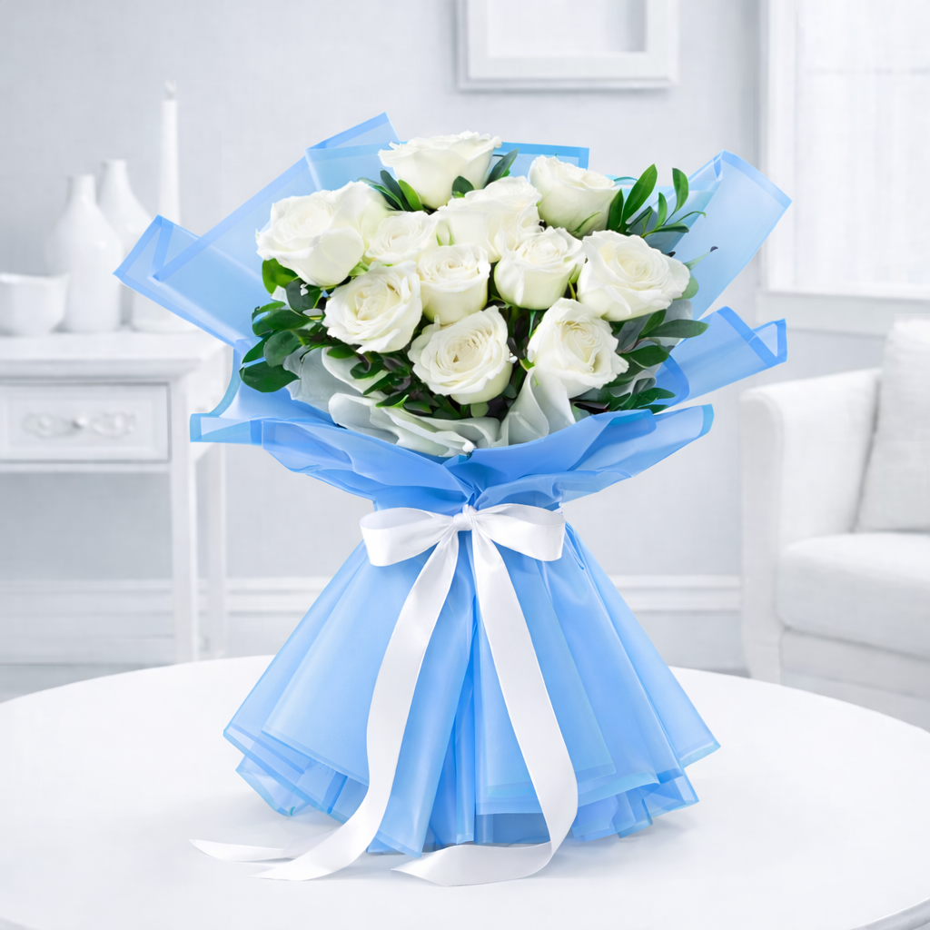White roses bouquet wrapped in blue organza and tied with a white satin ribbon on a white table.