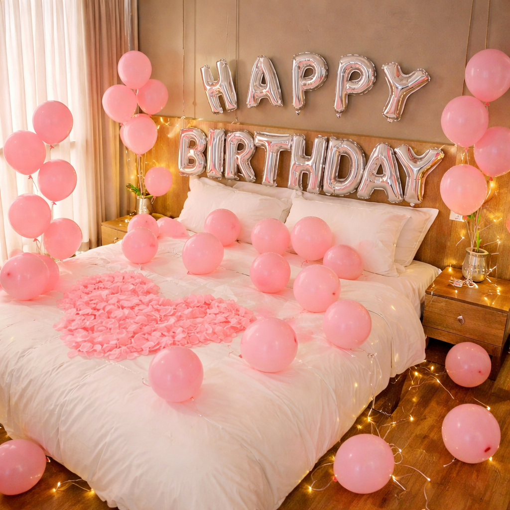 Birthday bedroom decoration with pink balloons, silver 'Happy Birthday' foil letter banner, rose petal heart on bed, and fairy lights.