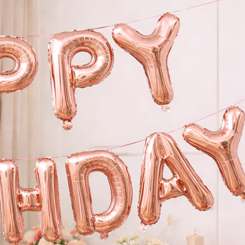 Close-up of rose gold 'Happy Birthday' foil letter balloons banner with flowers in the background