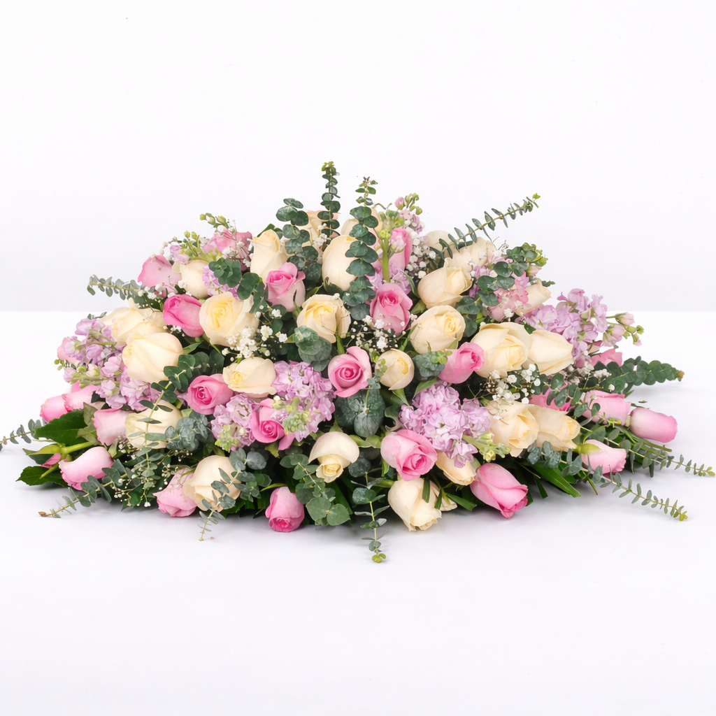 Large oval floral centerpiece with cream and pink roses, lavender stock flowers, baby's breath, and eucalyptus on a white background.