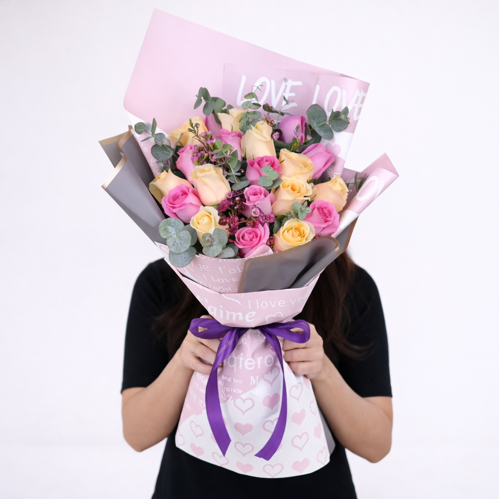 Woman holding a large mixed pink and cream rose bouquet wrapped in "Love" printed paper with a purple ribbon