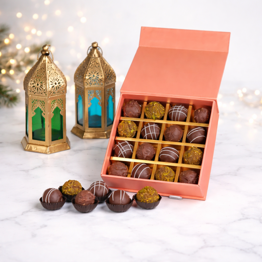 Open peach gift box of assorted chocolate truffles with two gold Moroccan lanterns and fairy lights in the background.