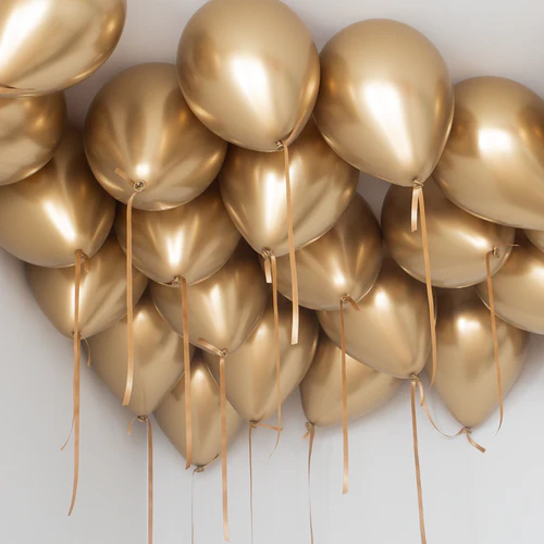 Cluster of chrome gold balloons with gold ribbons against a white wall.