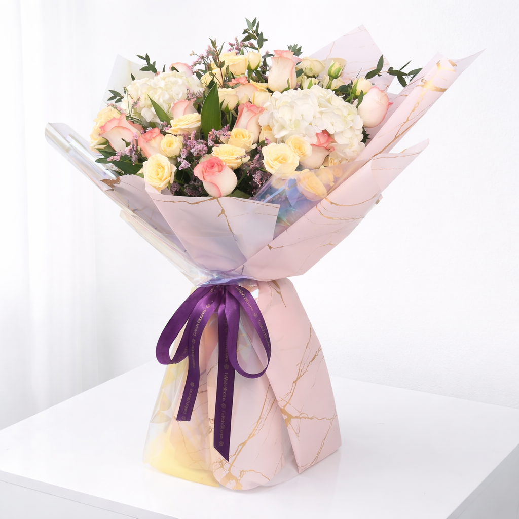 Luxury pink and cream rose bouquet in pink marble and iridescent wrapping on a white surface.