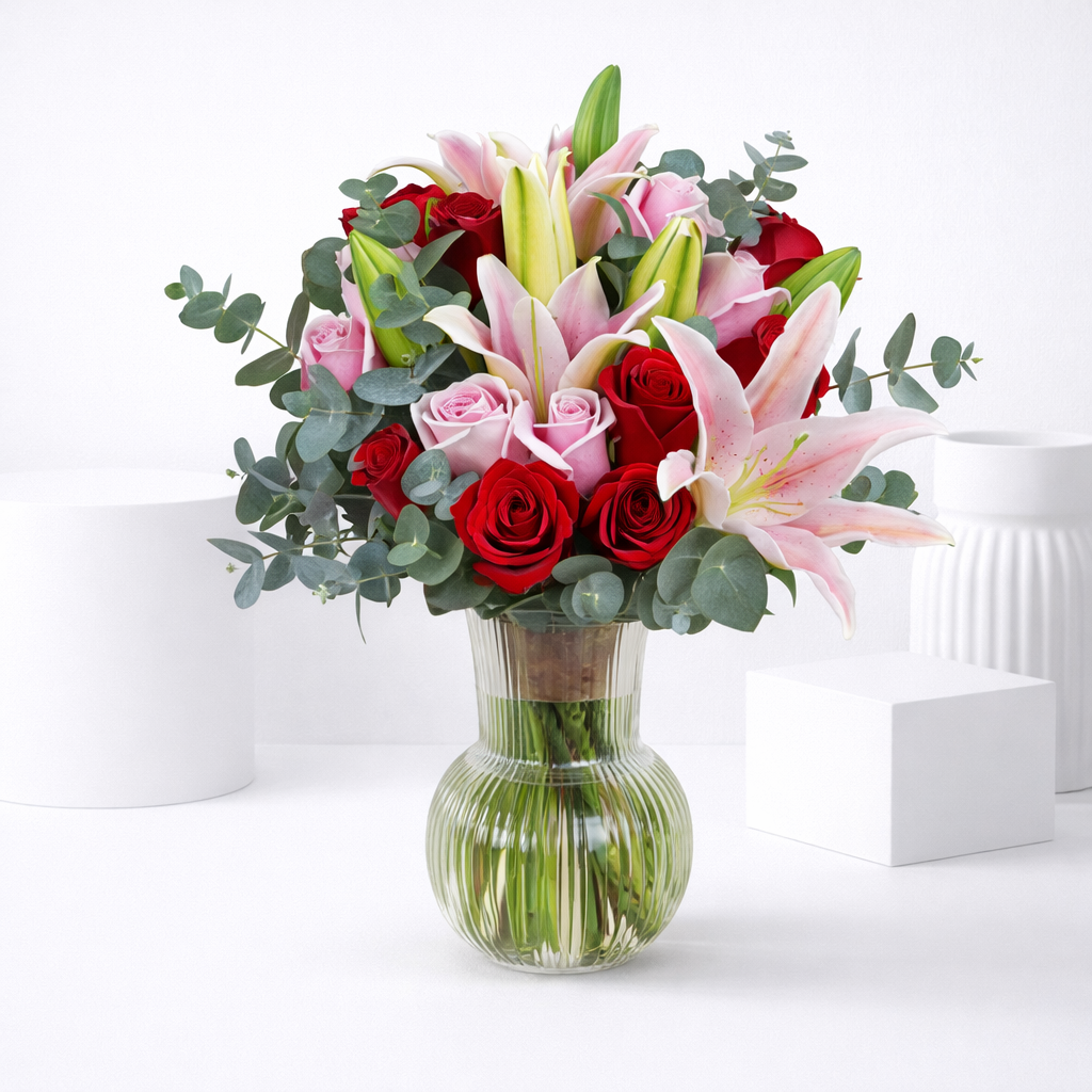 Red roses, pink roses, and pink lilies bouquet in a ribbed glass vase.
