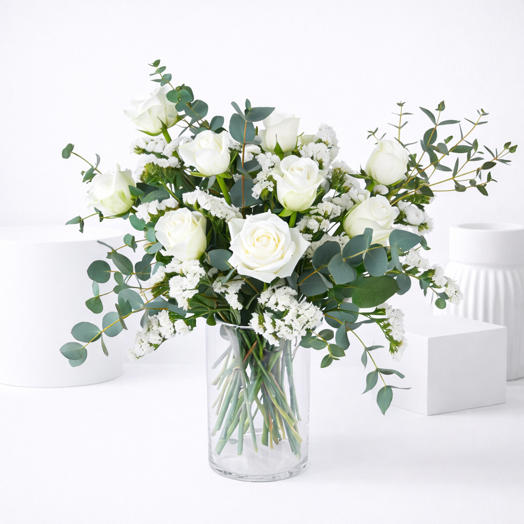 White roses and eucalyptus bouquet in a clear glass vase.