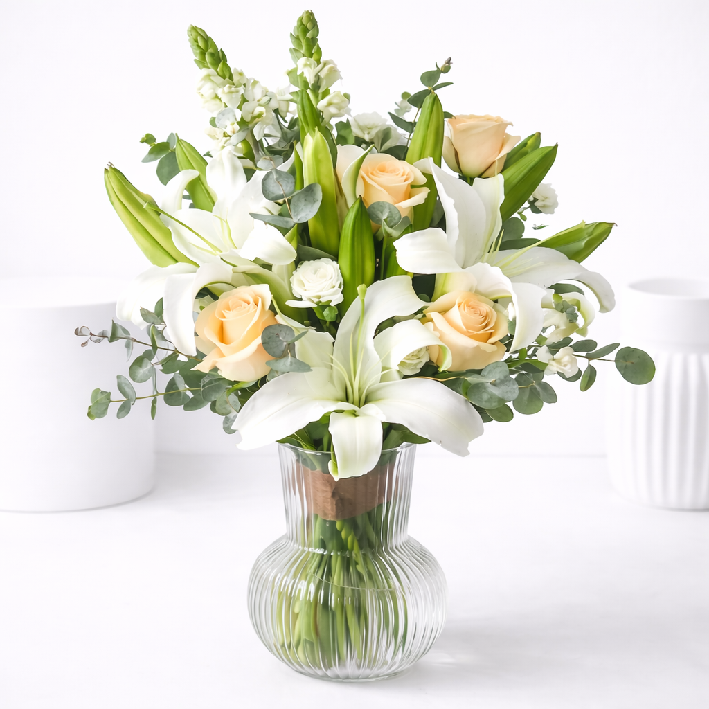 Close-up of white lilies and peach roses in a ribbed glass vase.
