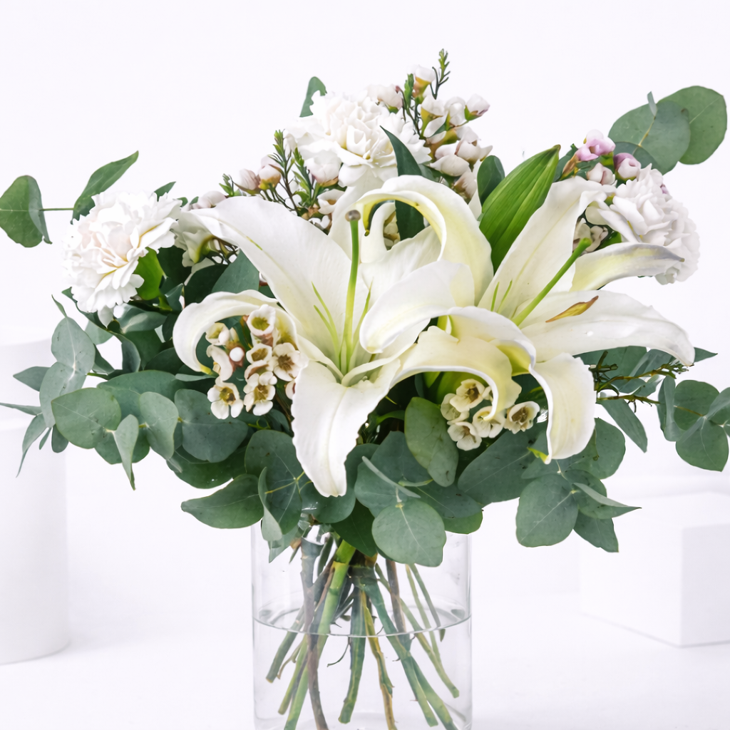 Close-up of white lilies, wax flowers, and carnations with eucalyptus in a clear glass vase.