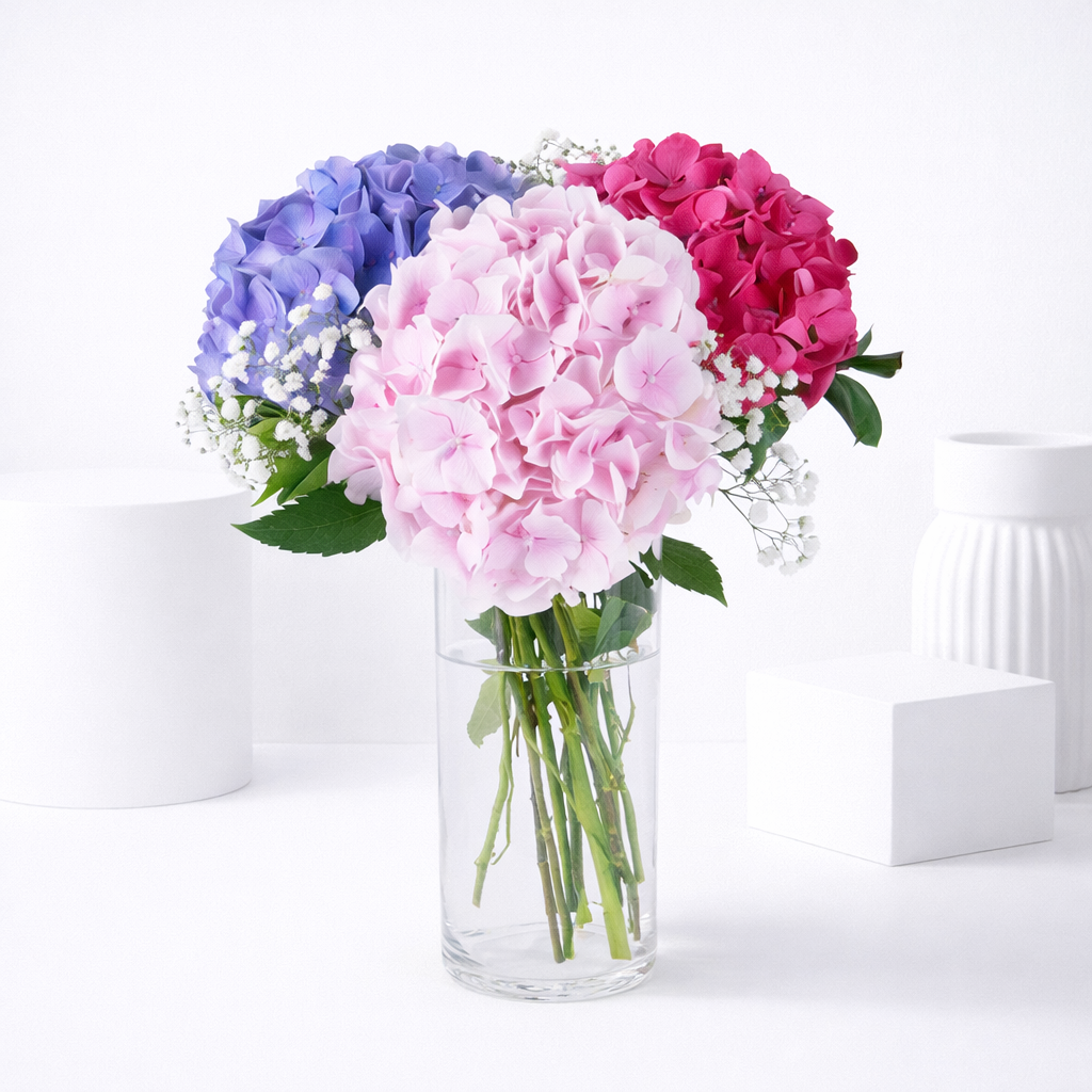 Pink, purple, and hot pink hydrangeas with white baby's breath in a clear glass vase.