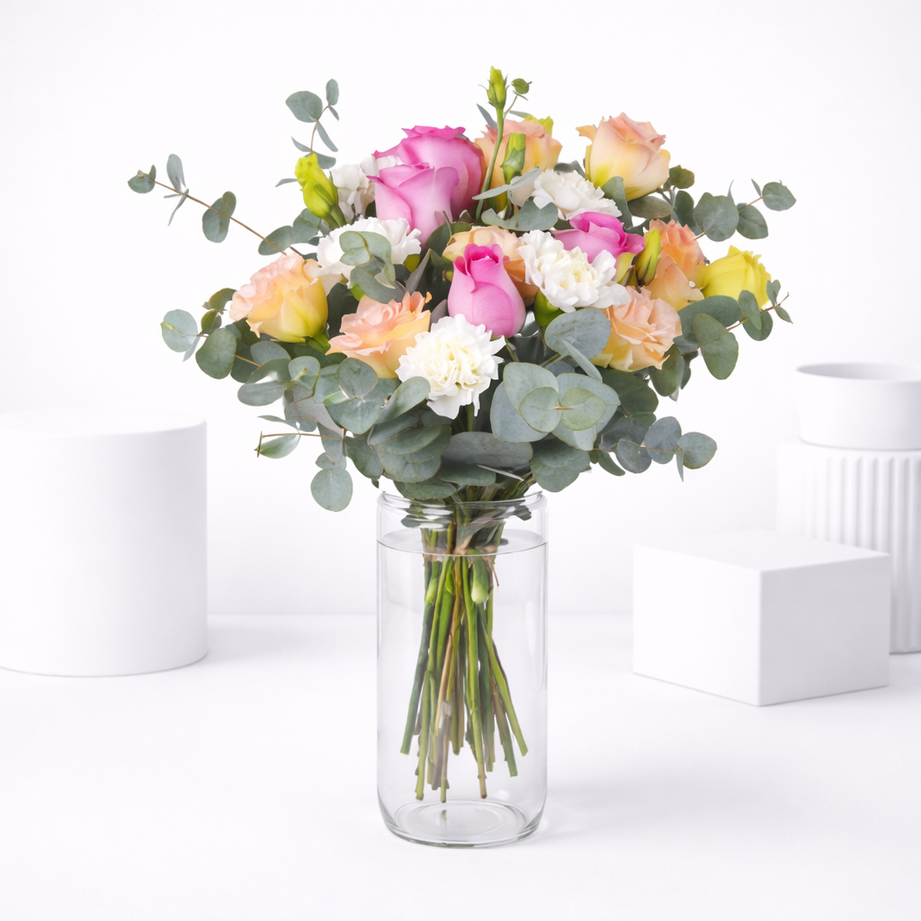 Pink, peach, and yellow roses with white carnations and eucalyptus arranged in a clear glass vase.