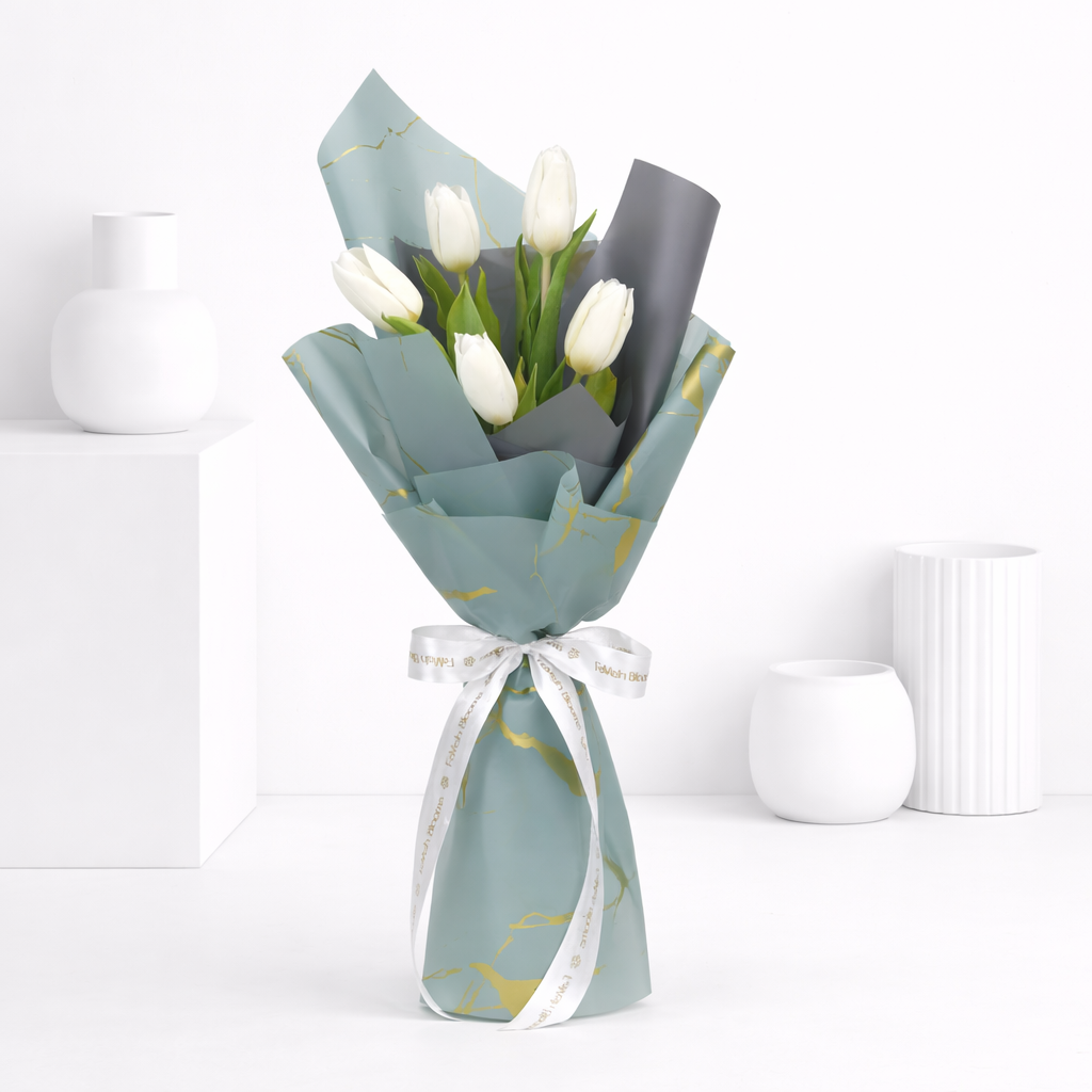White tulip bouquet wrapped in blue-grey and gold-print paper tied with a white Favish Blooms ribbon.