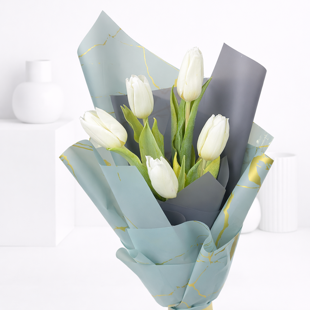 Close-up of white tulips in blue-grey and gold-print wrapping paper.