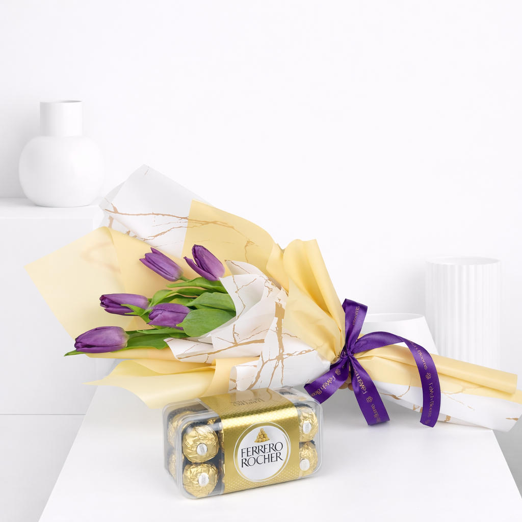 Purple tulip bouquet in gold and marble-print wrapping with a purple Favish Blooms ribbon, laid flat beside a box of Ferrero Rocher chocolates.