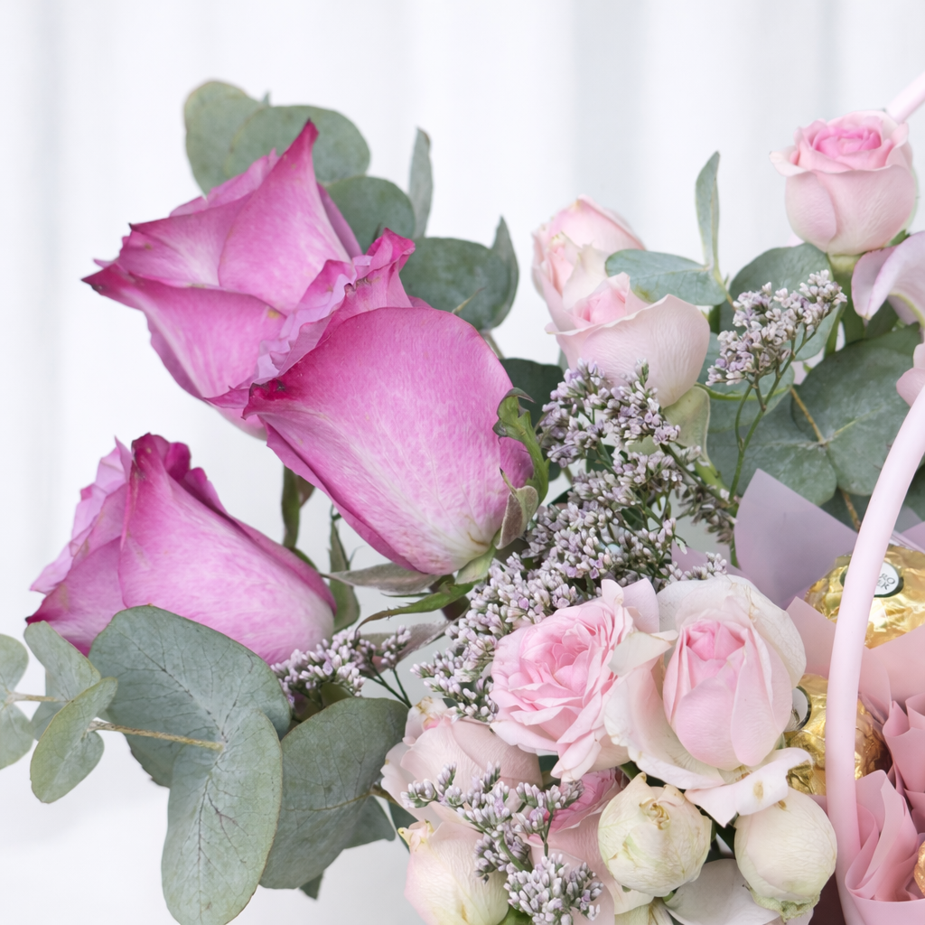 Macro shot of pink roses, soft pink spray roses, purple wax flowers, and eucalyptus with Ferrero Rocher chocolates visible in a pink quilted flower box.