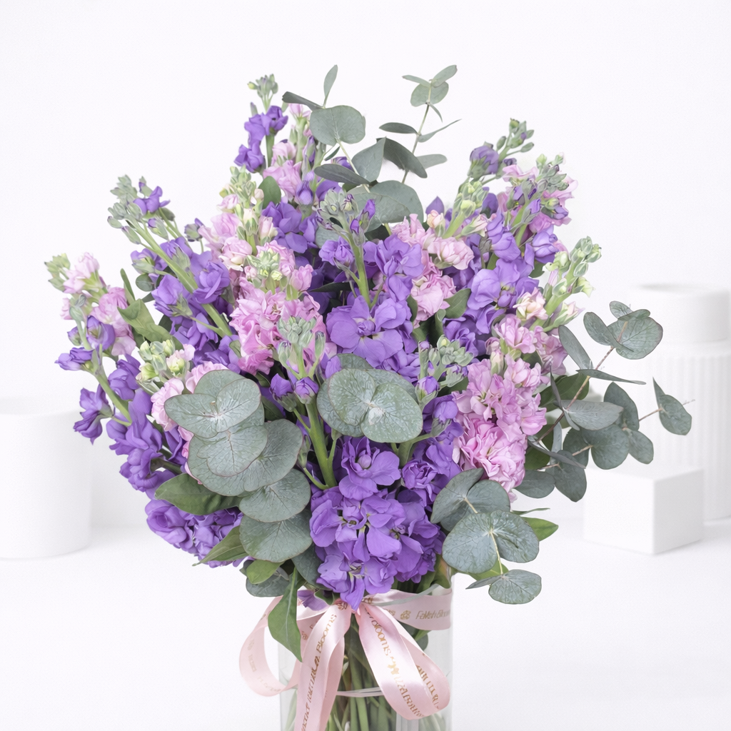 Close-up of purple and pink stock flowers with silver dollar eucalyptus in a ribbon-tied glass vase