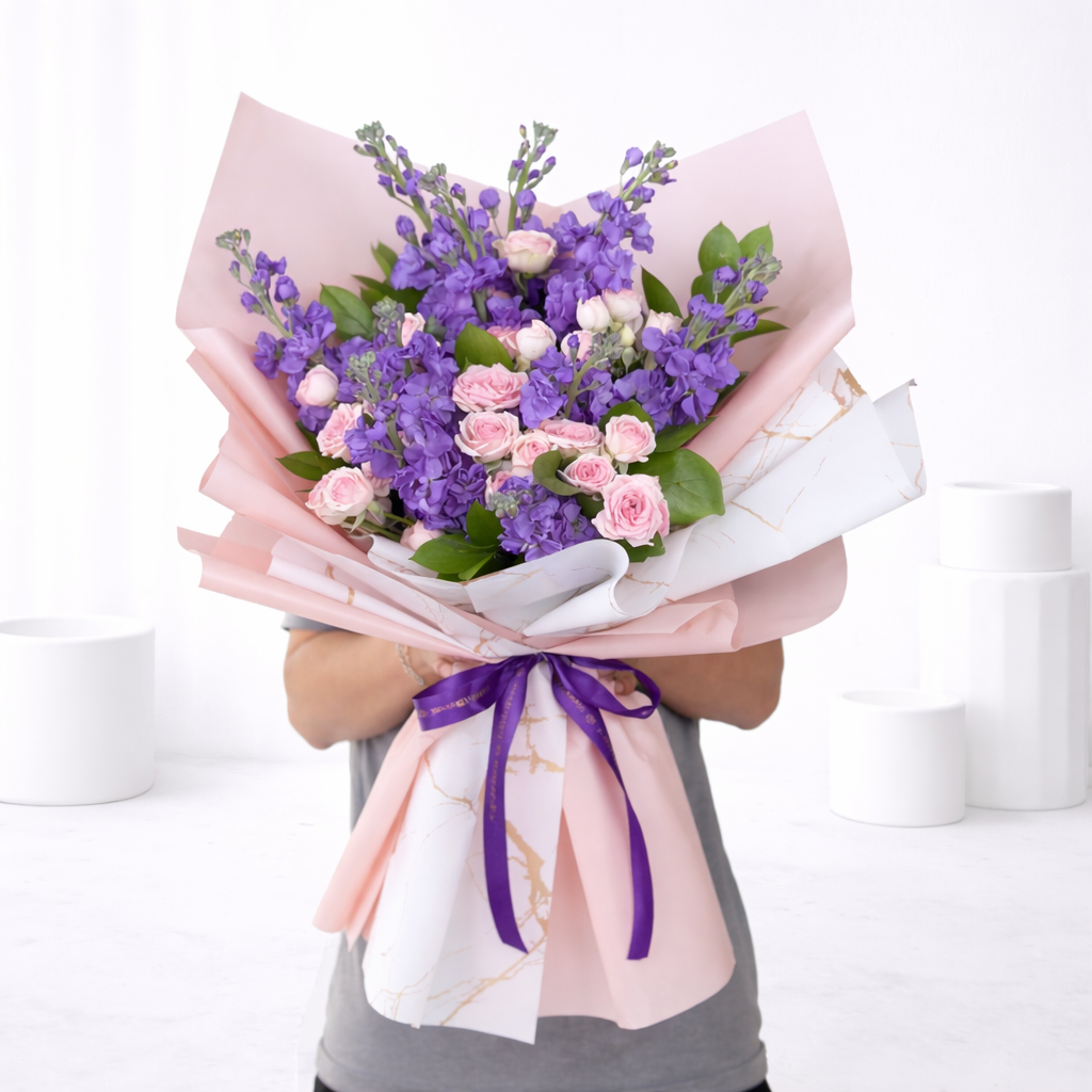 Person holding large purple stock and pink rose bouquet in pink marble wrapping with purple ribbon.