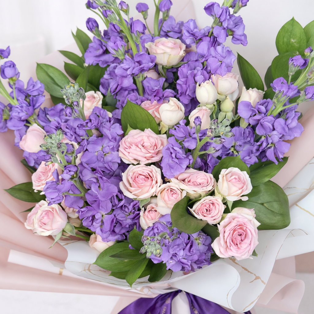 Close-up of purple stock flowers and pink spray roses bouquet with green leaves.