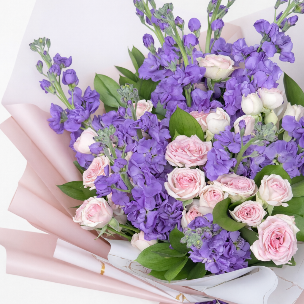 Overhead close-up of purple stock flowers and pink spray roses bouquet in pink marble wrapping.