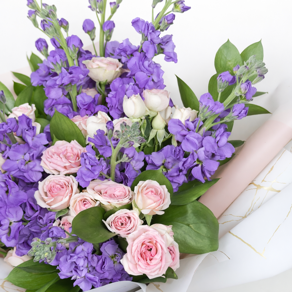 Detailed close-up of purple stock flowers and blush pink spray roses with green leaves.