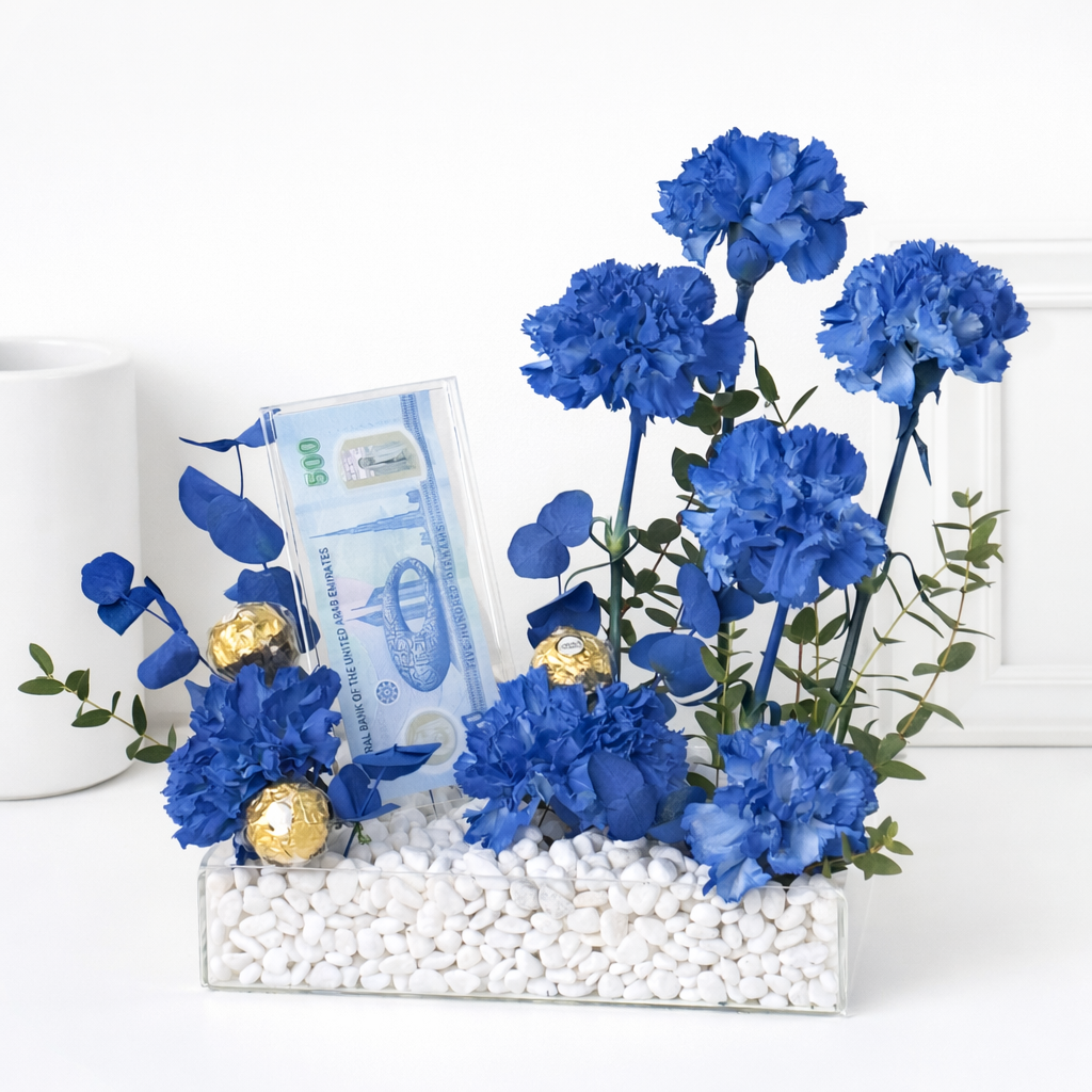 Blue carnation floral arrangement with Ferrero Rocher chocolates and a UAE 500 Dirham note in a clear acrylic tray.