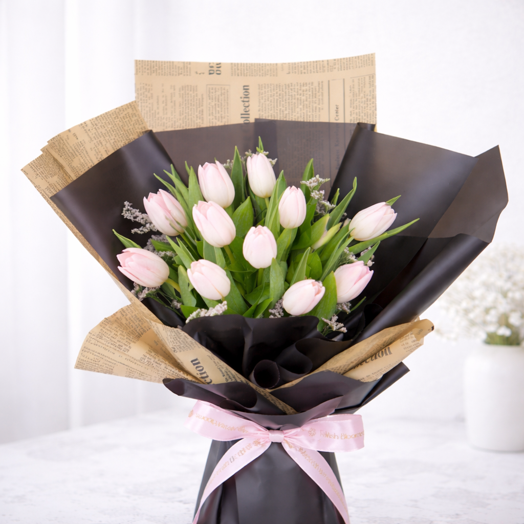 Soft pink tulip bouquet with lavender filler wrapped in black matte and newspaper kraft paper, tied with a FaVish Blooms pink satin ribbon.