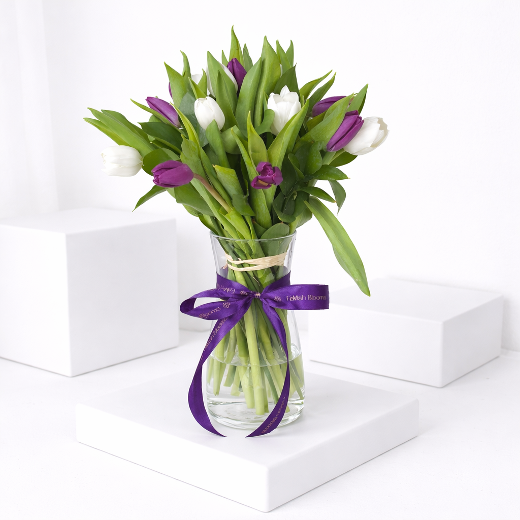 Purple and white tulips in a glass vase tied with a FaVish Blooms purple ribbon.