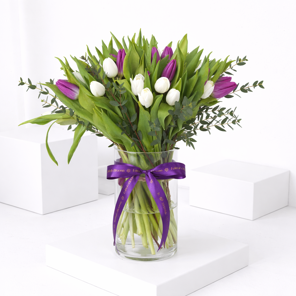 Purple and white tulips with eucalyptus in a glass vase tied with a FaVish Blooms purple ribbon.