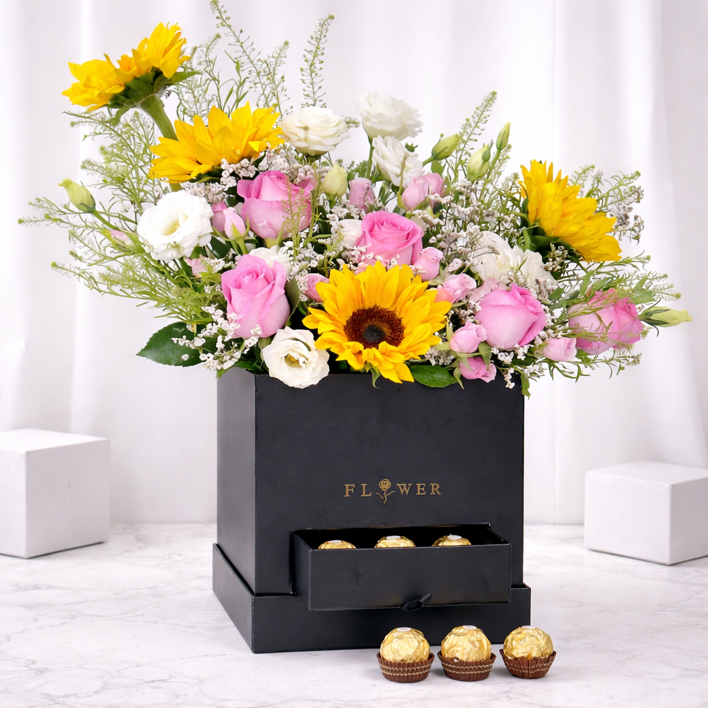 A black gift box with sunflowers, pink roses, and white lisianthus, with a pull-out drawer containing Ferrero Rocher chocolates.