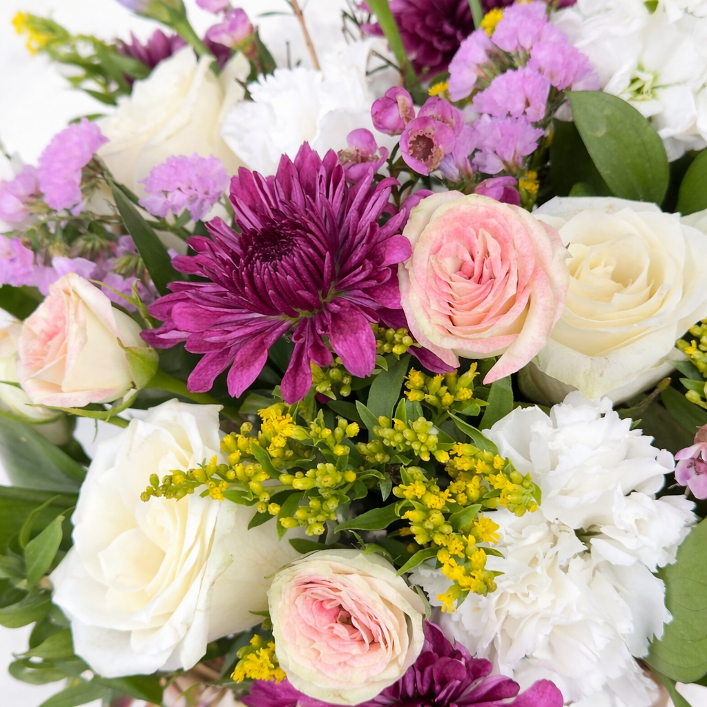 Close-up of purple chrysanthemums, pink and white roses, and yellow filler blooms in a mixed floral arrangement.