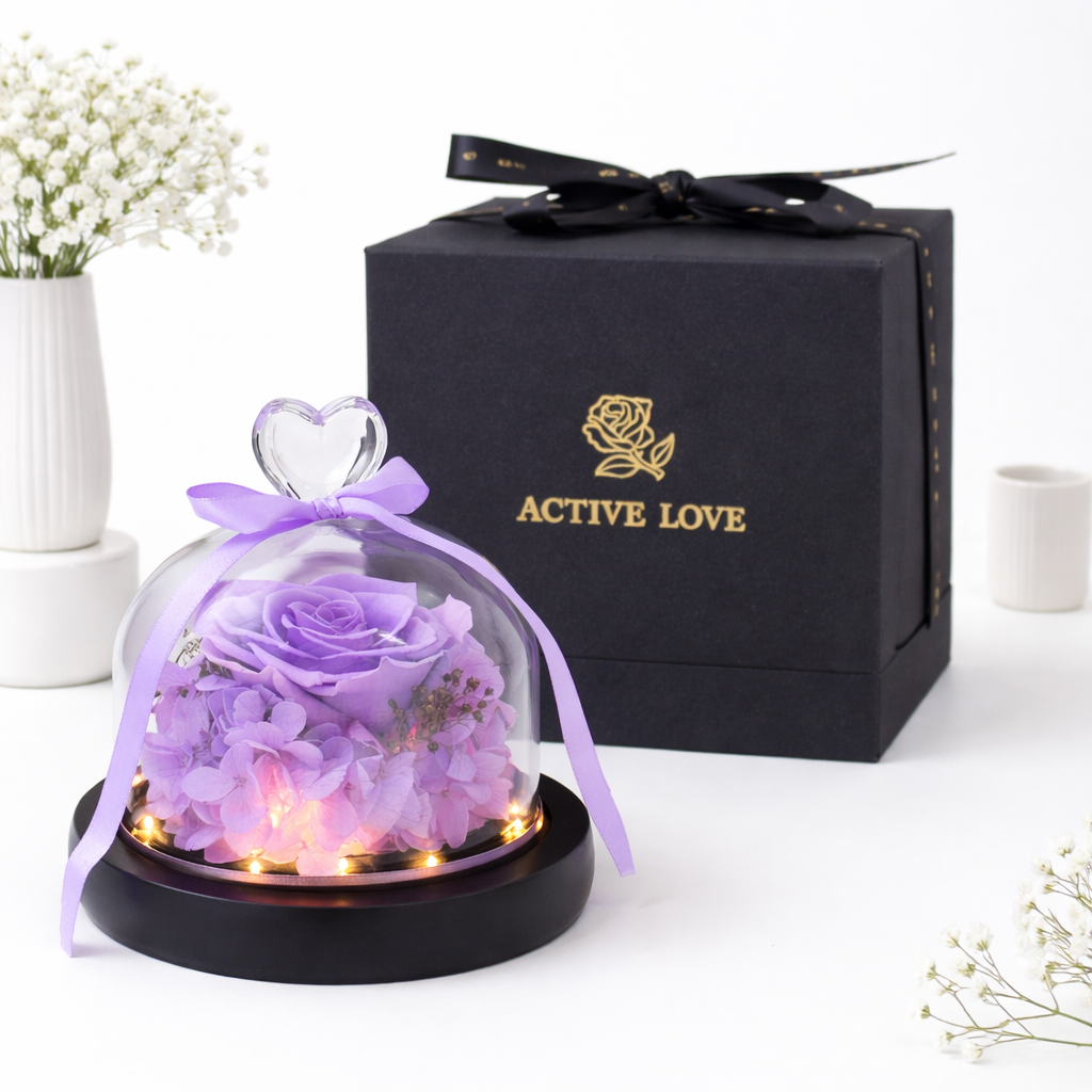 Purple preserved rose and hydrangeas in an LED-lit glass dome with a heart handle and ribbon, beside an "Active Love" black gift box.