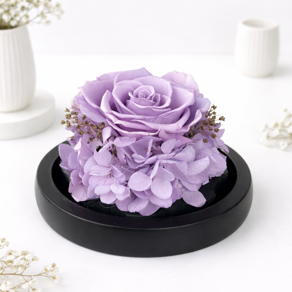 Close-up of a purple preserved rose surrounded by hydrangeas and dried filler flowers on a black round base.