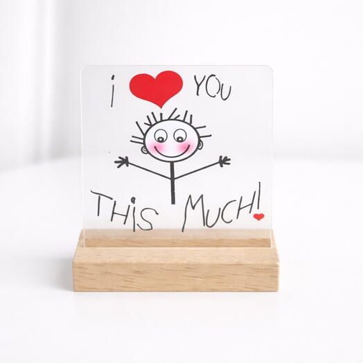 A card in a wooden holder featuring a stick figure with arms spread wide, text reading "I ❤️ You This Much!"