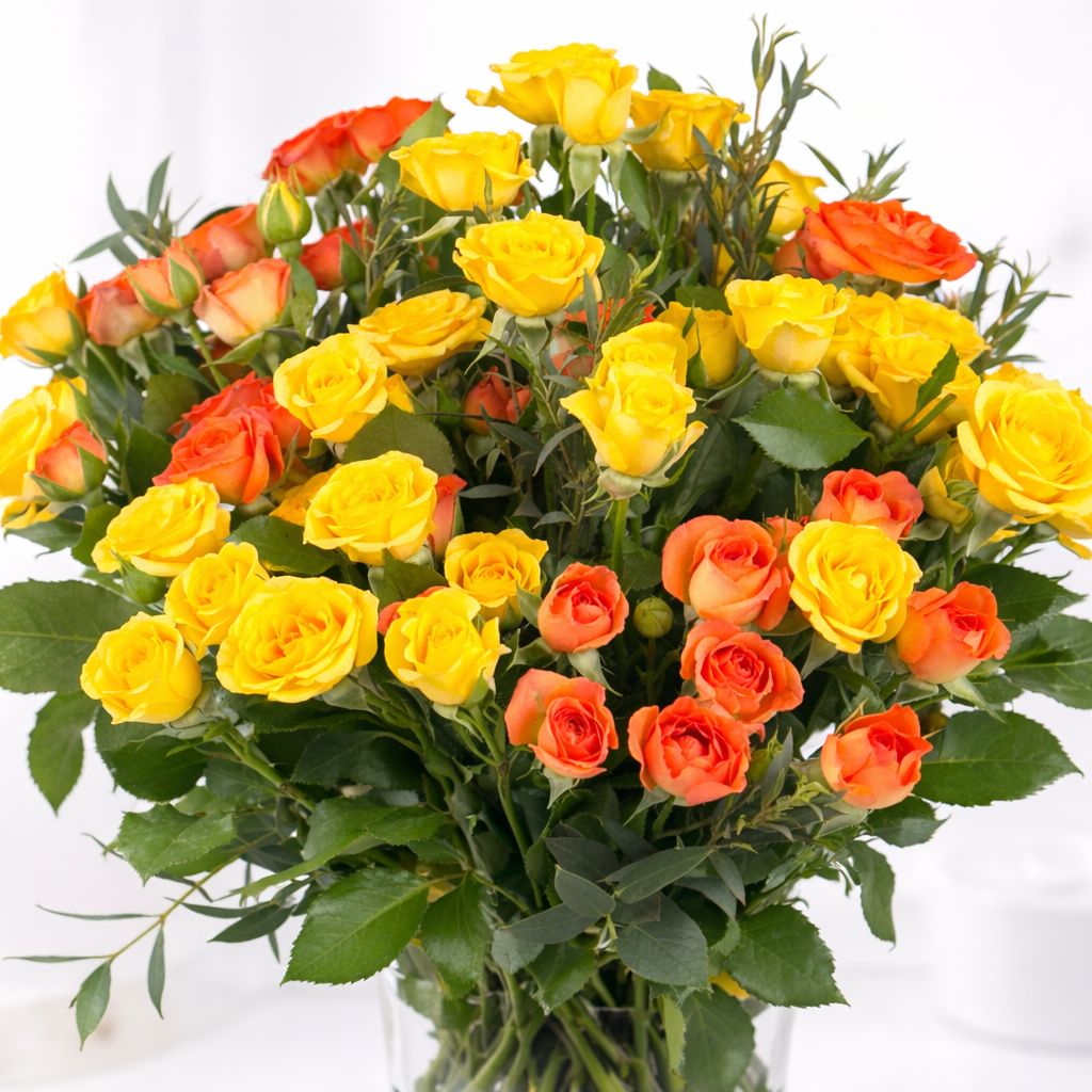 Close-up of yellow and orange roses with lush green foliage in a glass vase.