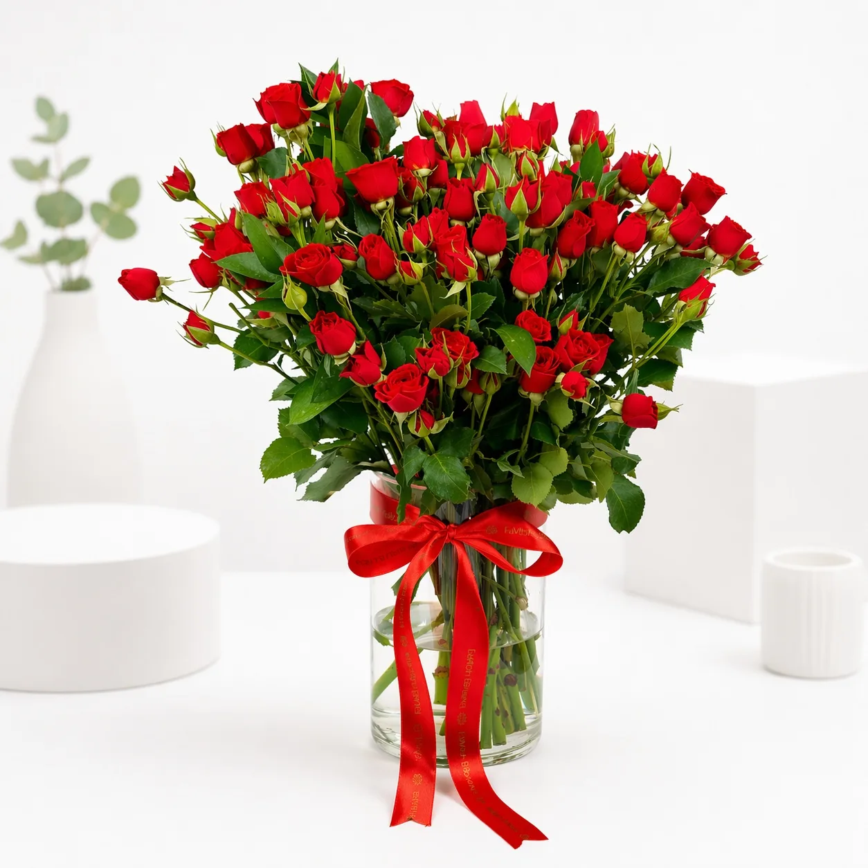 Lush bouquet of red spray roses in a glass vase tied with a red satin ribbon.