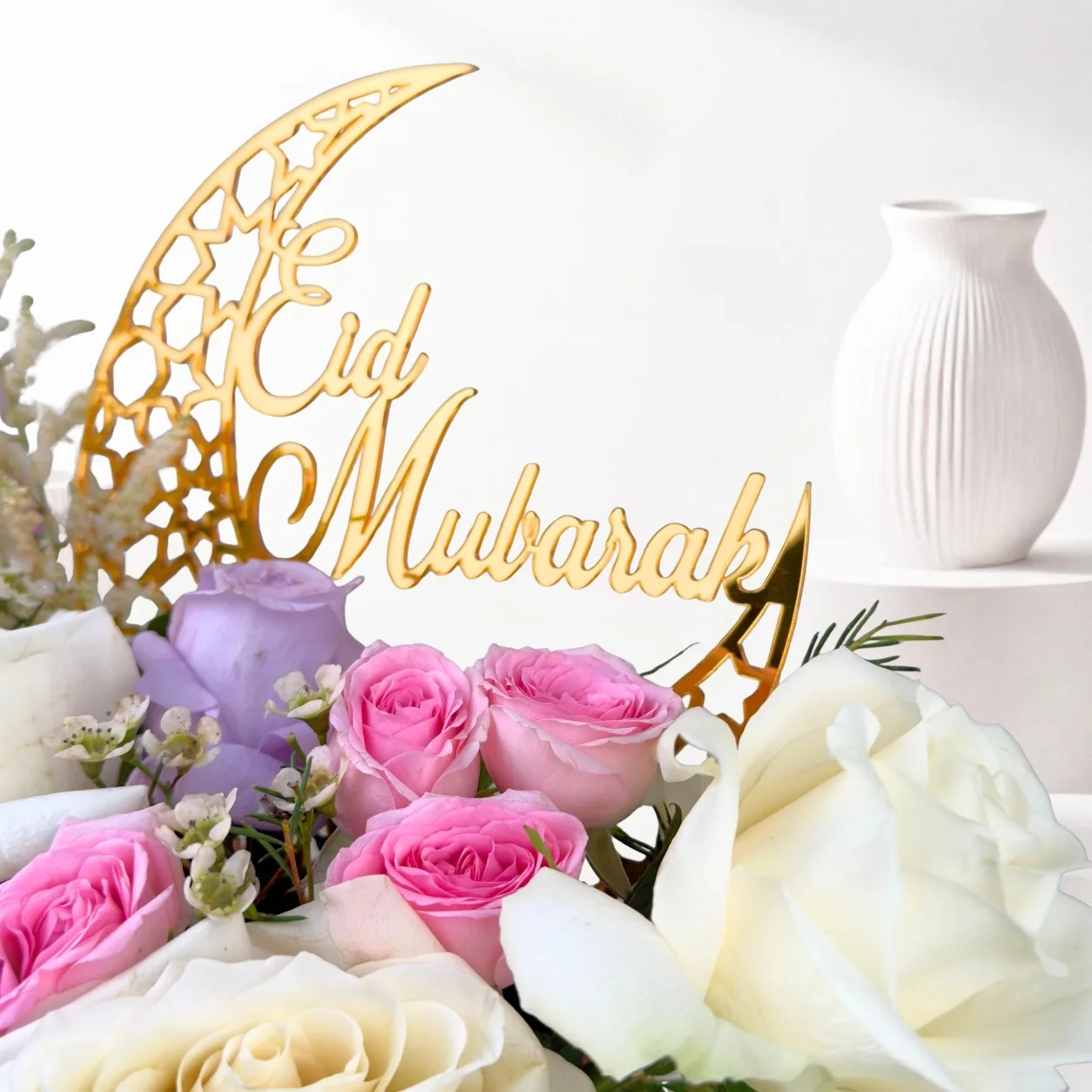 Close-up of an Eid Mubarak floral arrangement featuring white roses, pink roses, lavender roses, and a golden Eid Mubarak crescent topper.
