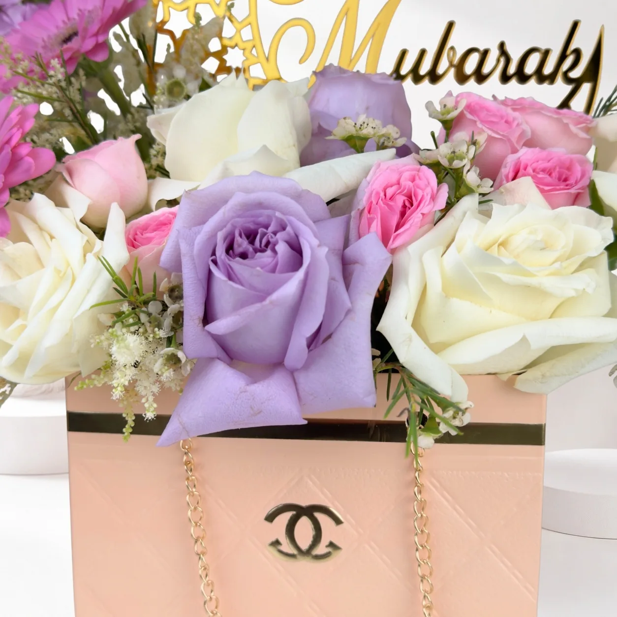 Close-up of a luxury Eid Mubarak floral handbag arrangement featuring lavender roses, white roses, pink spray roses, and a peach designer gift box with gold accents.