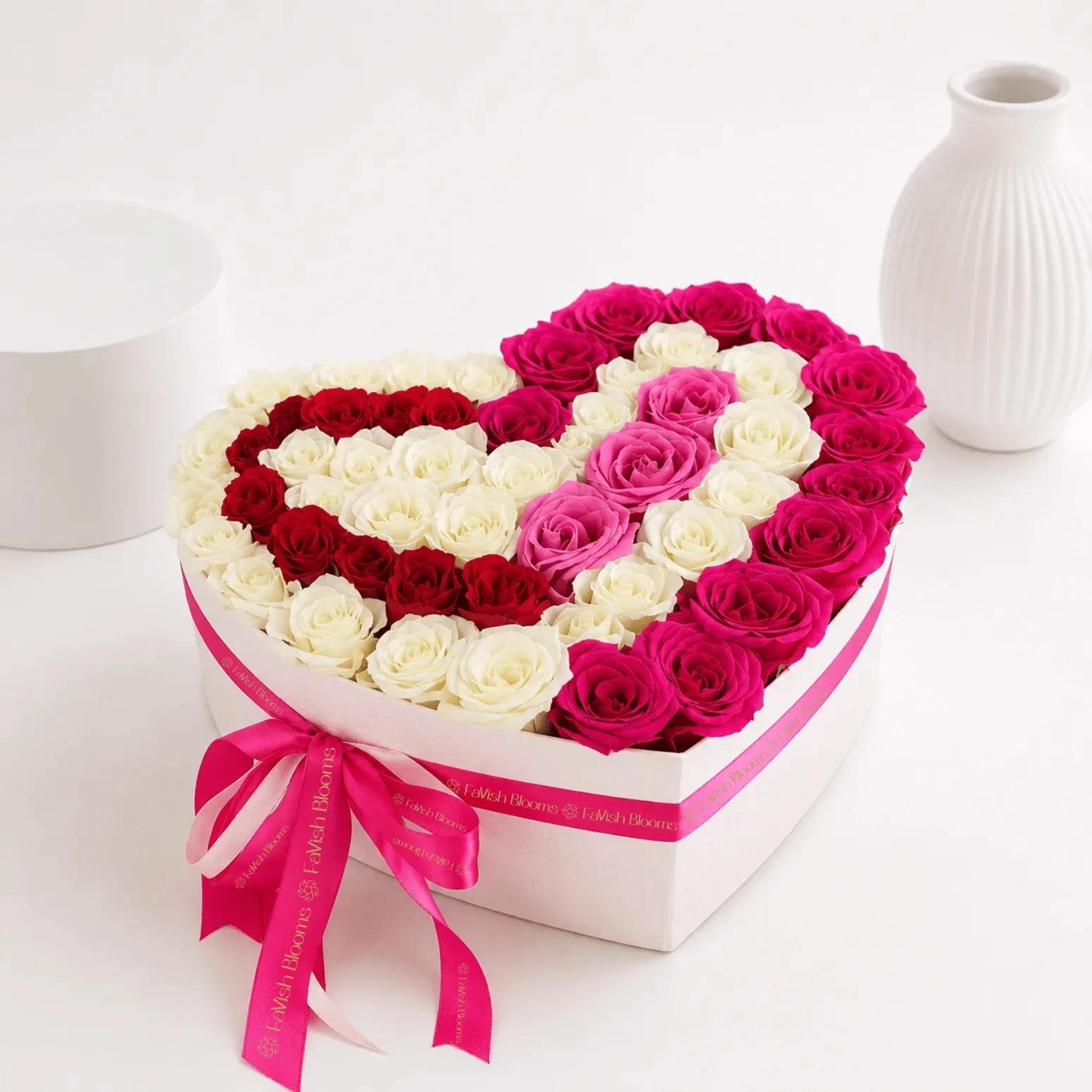 Luxury heart-shaped rose box featuring pink, white, and red roses arranged in a romantic design, finished with a pink Favish Blooms ribbon.